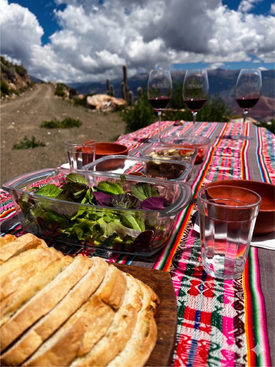 Mesa con textiles andinos, pan casero y copas de vino frente a los cerros